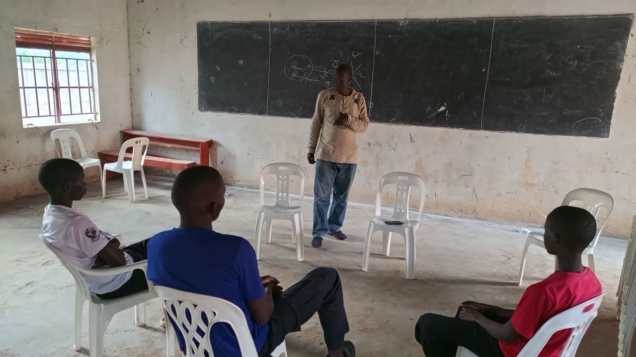 A BREFON facilitator leading a seated group counselling session with young people in a school classroom in Northern Uganda.